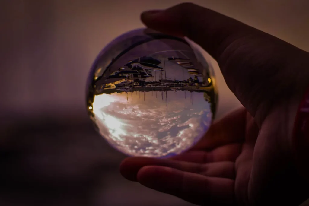 A hand holding a clear crystal ball that reflects an upside-down view of the scene behind it
